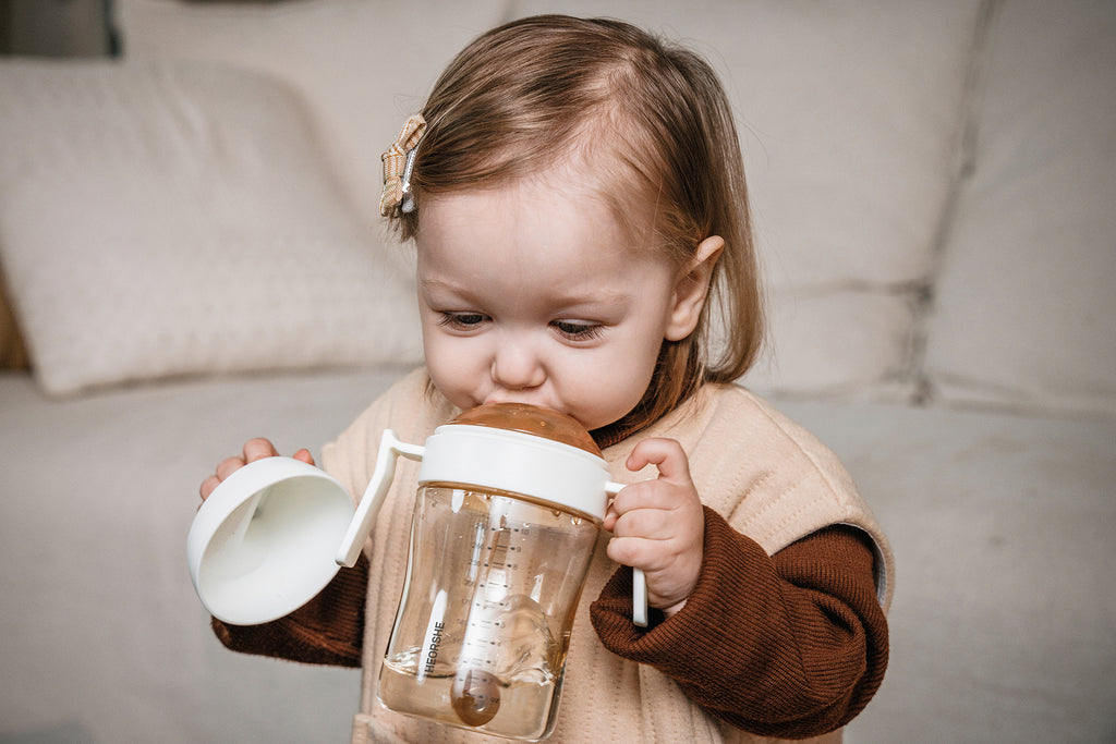 Child holding a sippy cup with a handle, sitting on a couch.