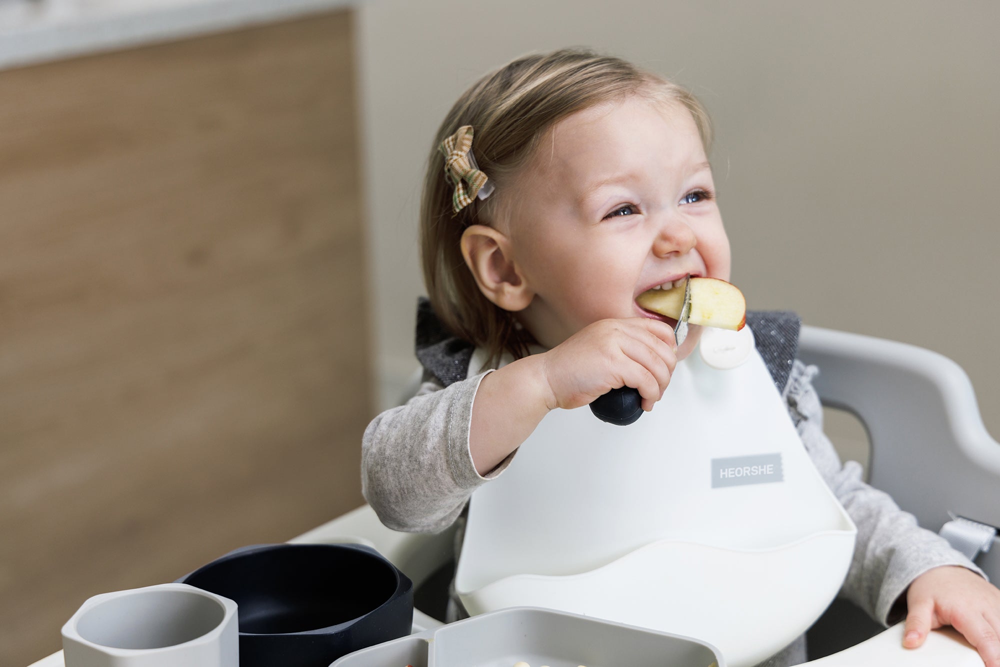 Child eating an apple in a high chair with a bib