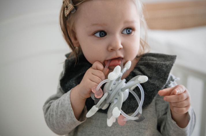 Baby holding a teething ring with a neutral background
